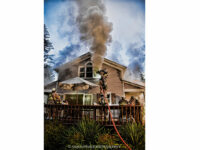 Firefighters manage a hoseline while on a ladder during the fire operations.