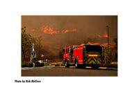 A fire apparatus with a line of fire burning in the background