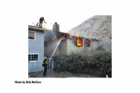 At the Tick Fire, firefighters direct a hosestream into a burning building