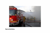 Fire apparatus with firefighters and streams with a helicopter in the background