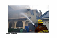 A Los Angeles County Fire Department member aims a hose stream onto a burning residence