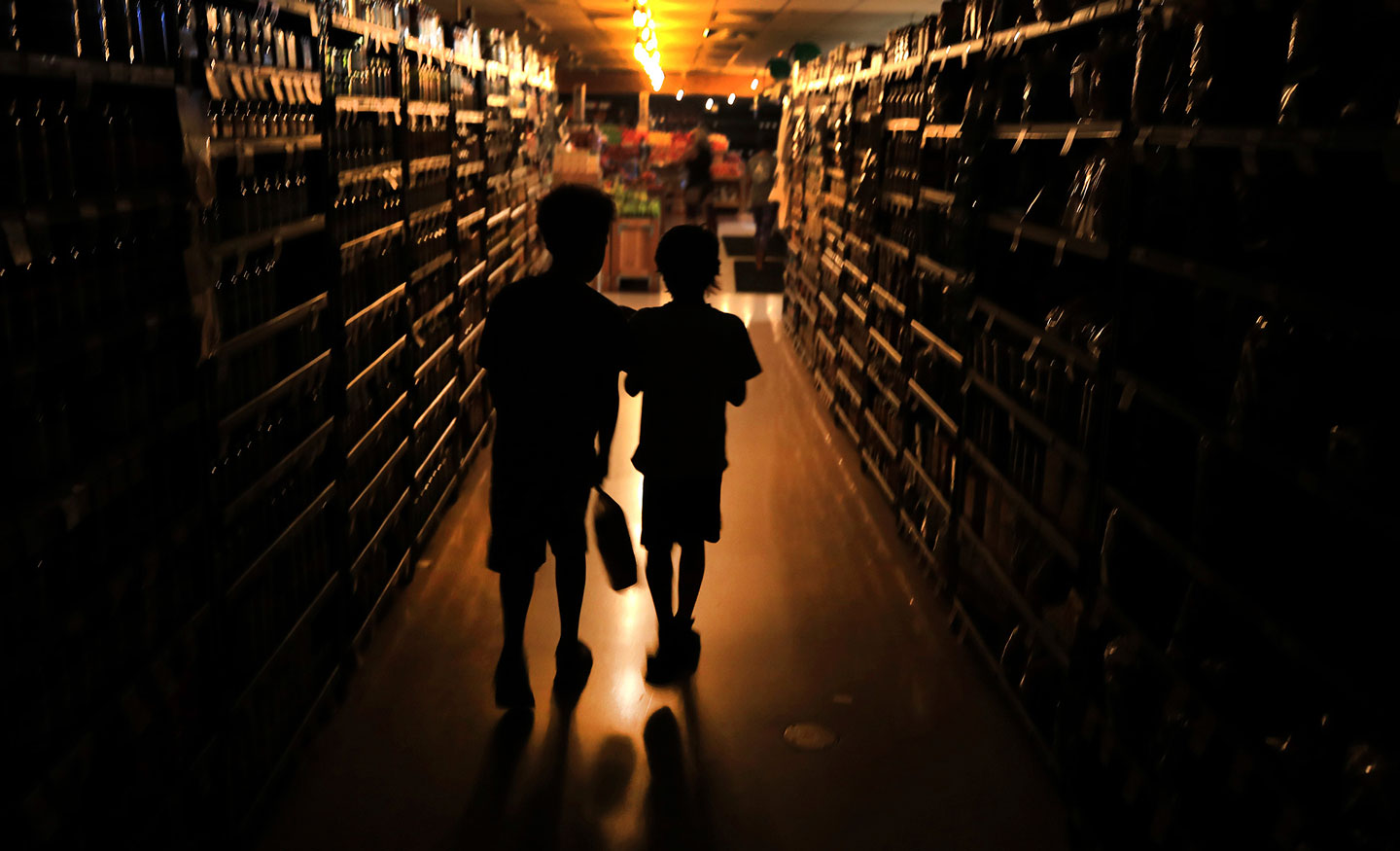 Elijah Carter 11, left, and Robert Haralson, 12, help shop for their parents in a darkened Olivers Supermarket in the Rincon Valley community, Wednesday, Oct. 23, 2019, in Santa Rosa, Calif. The west side of the store was lit by patio lights powered by a generator as power was shut off again by Pacific Gas & Electric Co. due to high fire danger. (Kent Porter/The Press Democrat via AP)