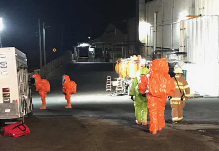 Two technicians enter dry decon (left) while Hazmat Assistant Chief DiPaolo escorts more technicians to the hot zone (right). In the background is the recovery vessel where the product was transferred (center).