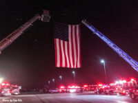 At night, a photo of the flag held between two fire apparatus