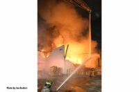 A firefighter applies a stream to the burning warehouse