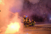 Several firefighters, surrounded by sparks, coordinate an exterior line