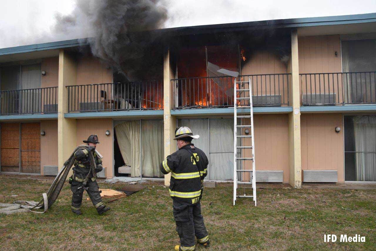 Firefighter brings hoseline to ground ladder at motel fire