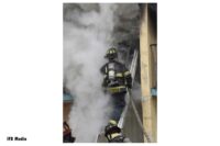 Firefighter stretches hoseline up a portable ladder to second-floor balcony