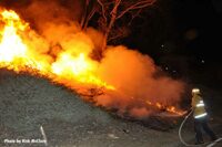 A firefighter operates a hoseline on a burning hill