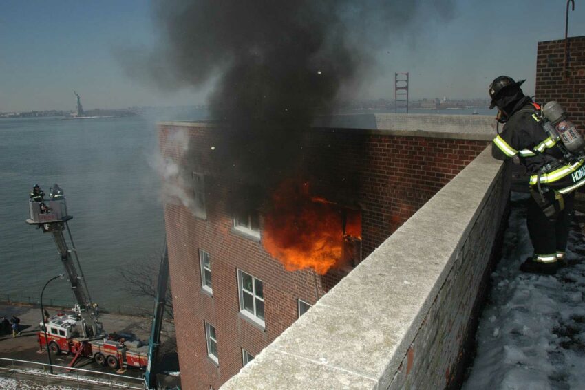 FDNY firefighter at abandoned apartment building in NYC watching fire and smoke blow out a window