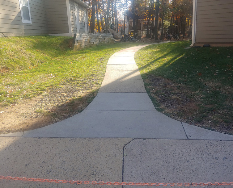 This fire lane is the only access to this garden apartment complex. Rubber matting is installed on both sides of the sidewalk to allow fire apparatus to drive down and access the building. The dirt and grass normally covering the matting washed away, exposing the matting.  