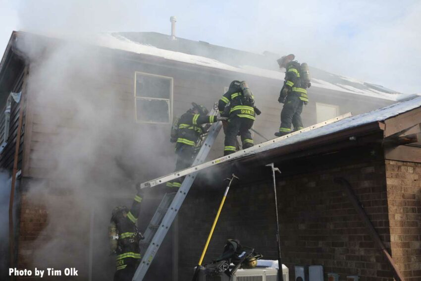 Firefighters ascend a ladder to the roof