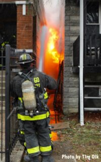 A firefighter uses a hose stream to limit fire spread to an exposure building