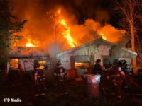 Firefighters work on the exterior of a burning home