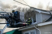 Smoke shoots from the windows as firefighters work in the bucket and on a roof at a house fire