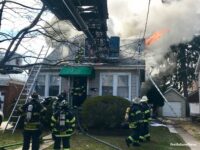 Fire vents from the upper floor of a home as firefighters work at the scene. A tower ladder is used at the scene.