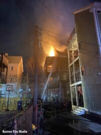 Firefighters direct water stream onto fire venting from upper part of home