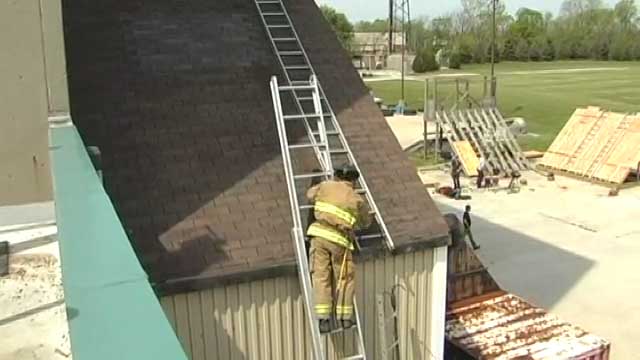 Firefighters on a ladder positions another ladder on the roof