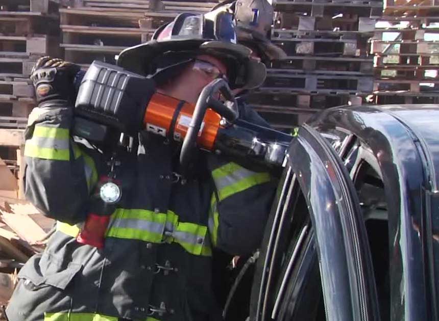 Firefighter with extrication tool attacking B post of vehicle