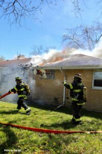 Firefighters moving hoselines as flames vent from the house fire