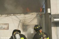 Firefighters confront flames shooting through the roof of the building