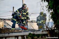 Multiple firefighters work the roof of a structure