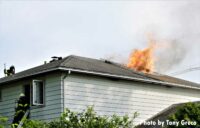 Firefighters operate at a house fire as flames show through the roof