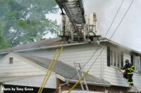 A tower ladder bucket with firefighters on ladders at the house fire