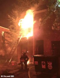 A D.C. firefighter advances toward a building as flames shoot from it