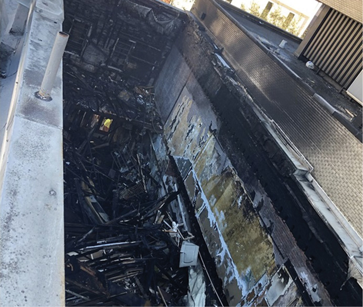 The postfire results as seen from the third-floor roof of the D exposure and toward the B exposure’s fourth-floor deck, where we placed defensive and exposure lines. Looking closely at the A-side wall, you can see two windows, which were covered by lap siding. Roof crews also noted the only dead load on the roof was a residential air-conditioning unit. This may have been beneficial in preventing an earlier collapse. 