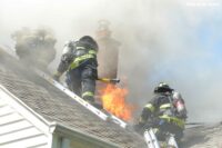 Firefighters move as flames erupt from the roof