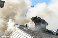 Firefighter on the roof of a home with smoke billowing about him