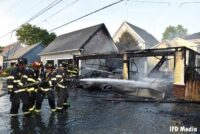 Firefighters work a hoseline on a charred out garage