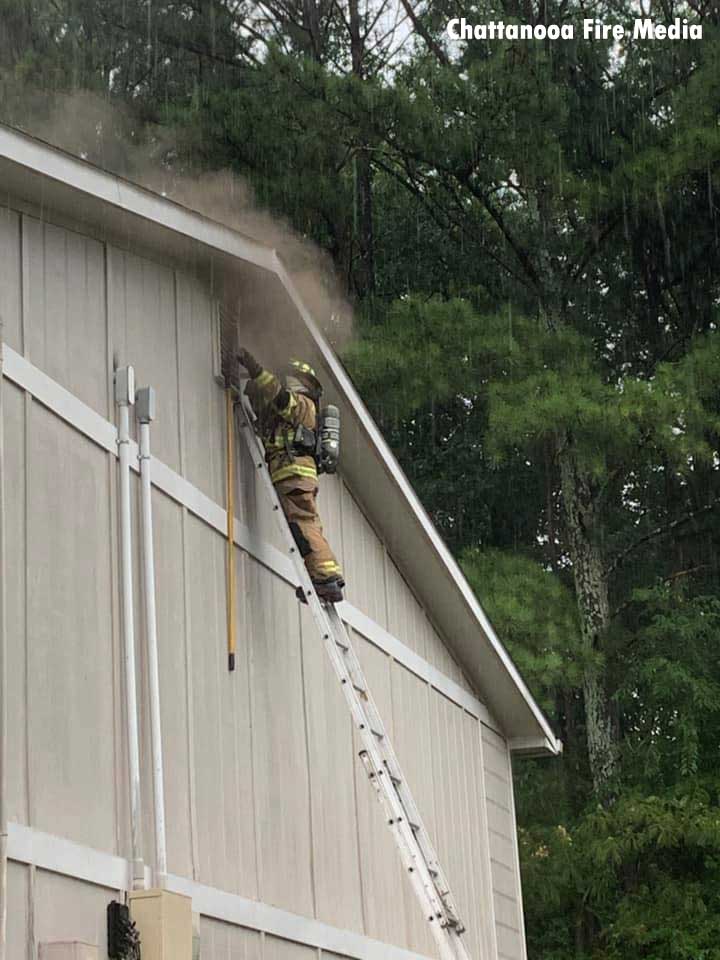 A firefighter on a ladder at a window filled with smoke