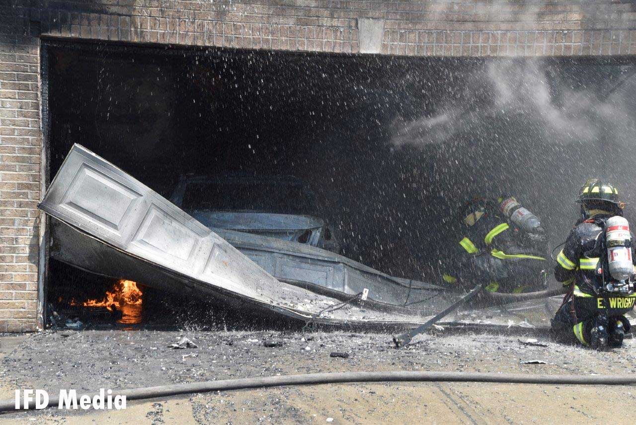 Indianapolis firefighters operating with a garage door and flames inside