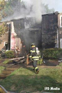 A firefighter advances toward a building with smoke showing