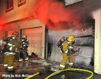 Smoke shoots from a garage as an LAFD firefighter attempts to gain entry