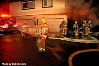 Firefighters bring a ground ladder as other members in the background use hoseline in garage