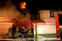 Firefighters on a hoseline put water in the garage as flames vent from a room above