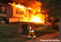 A firefighter near a fence as flames shoot from the structure