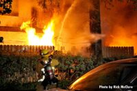 Firefighter with a hose as flames burn in the background