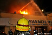 LAFD firefighter with helmet and fire raging in the building behind