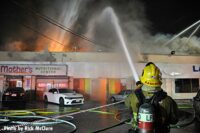 A City of Los Angeles firefighter with a hose putting water on the flames shooting from a building