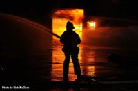 Firefighter with a hoseline framed by flames