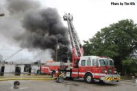 Dark smoke rising from building with tower ladder in operation