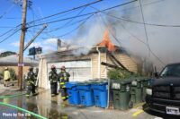 Firefighters with flames shooting from the top of a garage