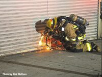 Firefighter with a power saw cutting through a metal roll-down gate