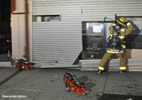 Firefighte rmaking multiple cuts in metal roll-down gate for forcible entry at fire