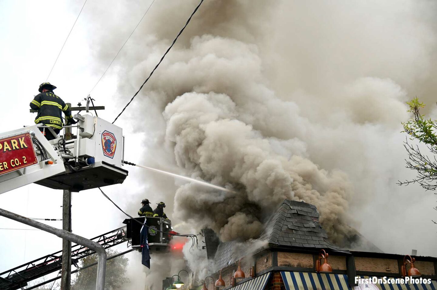 Firefighters in tower ladder buckets working as smoke rises from structure fire