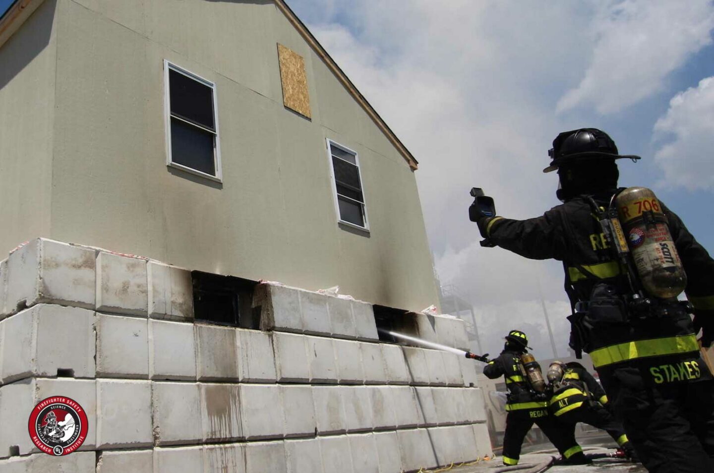 Firefighter with a TIC on exterior of structure while firefighter puts hose stream through opening